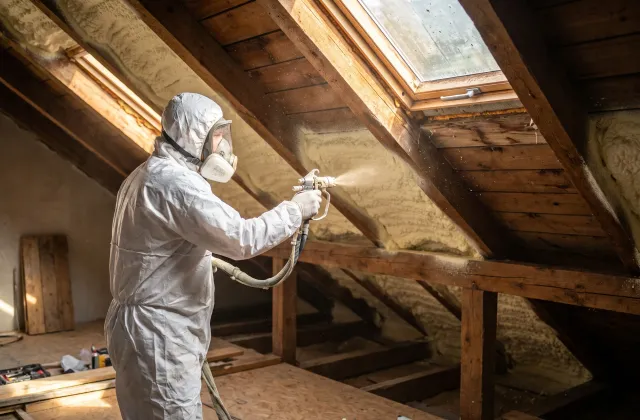 Technik v ochranném obleku a respirátoru nanáší stříkanou PUR pěnu na krokve